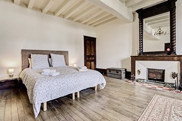 Grande chambre avec cheminée en pierre et poutres apparentes au Château de Juvardeil